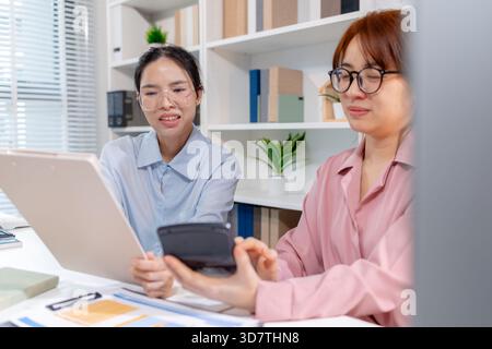 Deux collègues féminines discutent de rapports d'entreprise ensemble dans un environnement de bureau moderne, représentant le travail d'équipe, l'analyse de données et la collaboration Banque D'Images