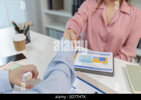 Deux femmes d'affaires asiatiques se serrant la main après avoir réussi une réunion dans un bureau moderne. Le geste représente le travail d'équipe, l'accord et le prof Banque D'Images