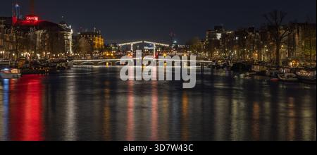 Vue panoramique de nuit sur la rivière Amstel à Amsterdam. La prise de vue longue exposition capture les ponts éclairés, les maisons de canal et les reflets lumineux. Amste Banque D'Images