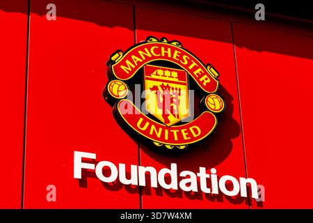 Manchester, Angleterre - 17 août 2025 : gros plan de l'écusson de la Manchester United Foundation affiché sur un mur rouge vif du stade. Banque D'Images