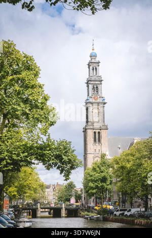 Haute tour de l'horloge dans une ville européenne avec des arbres et un canal sous un ciel nuageux. Amsterdam,. Pays-Bas Banque D'Images