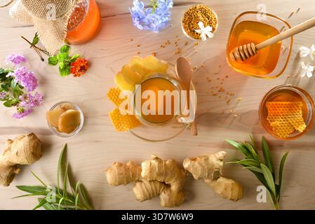 Infusion de gingembre et de miel sur une table en bois au centre avec des produits autour tels que des racines de gingembre, des pots de miel, du pollen et une décoration en nid d'abeille Banque D'Images