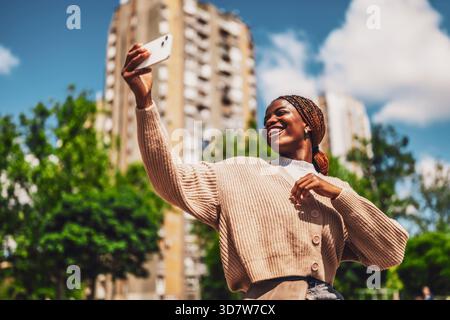 Jeune femme Noire heureuse prend selfie un jour ensoleillé avec son smartphone. Banque D'Images