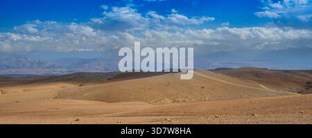 Vaste paysage désertique avec des collines ondulantes sous un ciel bleu vif avec des nuages dispersés. Désert d'Agafay, Marrakech-Safi, Maroc Banque D'Images