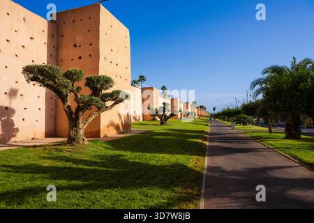 Remparts historiques de la ville avec des tours et des pelouses vertes luxuriantes sous un ciel bleu clair. Marrakech, Maroc Banque D'Images