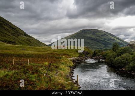 Paysage spectaculaire mettant en vedette une rivière serpentant à travers des collines verdoyantes sous un ciel nuageux. Glencoe, Écosse Banque D'Images