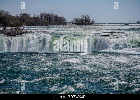 Une vue imprenable sur les rapides supérieurs des chutes du Niagara alors que les eaux turquoises débordent au-dessus des cascades par une journée de printemps claire. Arbres et petite île Banque D'Images