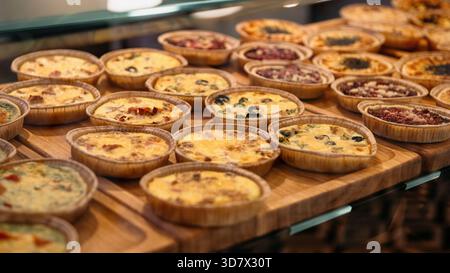 Gros plan de nombreuses mini-tartes et quiches fraîchement préparées sur un panneau d'affichage en bois. Nombreuses tartes aux garnitures salées (fromage, olives) Banque D'Images