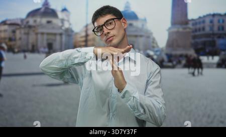 Un jeune homme hispanique portant des lunettes fait un geste de temporisation avec les mains devant le bâtiment du vatican ; sérénité. Banque D'Images