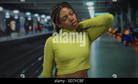 Femme tenant le cou avec la main montrant des douleurs au cou et exposé le milieu à un quai de train à l'intérieur d'un bâtiment ; inconfort. Banque D'Images