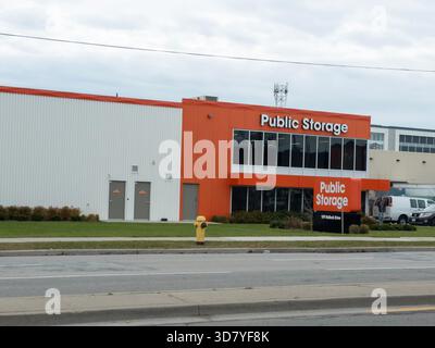 Bâtiment de stockage public avec façade orange et blanche, signalisation, aménagement paysager, bouche d'incendie et fourgonnette garée. Banque D'Images