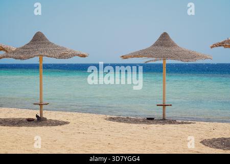Parasols ou parasols de paille sur une plage vide près de la mer, journée ensoleillée Banque D'Images