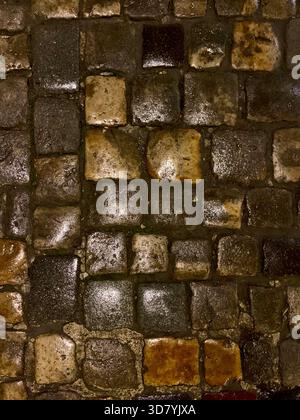 Fond mouillé de texture de chaussée pavée de rue avec des reflets lumineux la nuit Banque D'Images