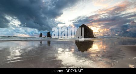 Coucher de soleil à couper le souffle à Haystack Rock sur Cannon Beach avec le ciel coloré et les reflets de l'eau calme sur la plage Banque D'Images