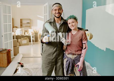Jeune couple multiethnique peignant le mur et rénovant la nouvelle maison ensemble Banque D'Images