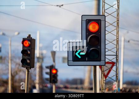 Feux de circulation modernes à l'intersection avec feu stop rouge vif et flèche directionnelle verte active sur fond de ville flou et câble de service Banque D'Images