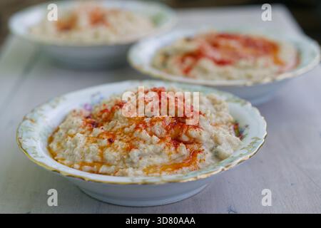 Houmous crémeux maison servi dans des bols en céramique anciens garnis de paprika et d'huile d'olive sur une table rustique en bois Banque D'Images
