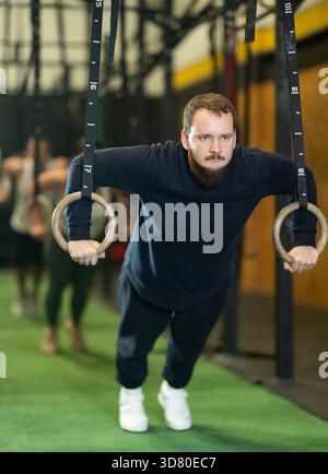 Gars barbu effectuant des pompes dans des anneaux de gymnastique au gymnase Banque D'Images
