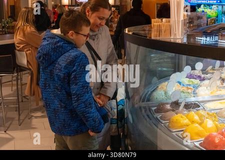 Mère et fils choisissant des saveurs de crème glacée au comptoir d'affichage de gelato dans un café occupé regardant des variétés colorées. Concept de sortie dessert en famille, swee Banque D'Images