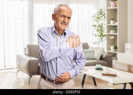 Homme âgé à la maison ressentant une douleur à l'épaule Banque D'Images
