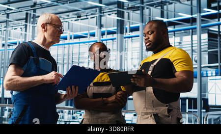 L'ingénieur principal de l'usine photovoltaïque d'industrie 4,0 lisant la paperasse discute avec les travailleurs pour maximiser la production d'énergie. Panneaux solaires SMART usine leader expérimenté donnant des tâches aux techniciens, caméra A. Banque D'Images