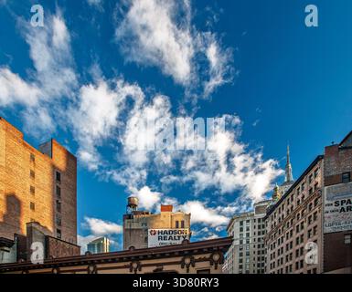 La lumière matinale projette une lueur chaude sur les bâtiments de Midtown Manhattan sous un ciel bleu vif rempli de nuages blancs moelleux. Banque D'Images