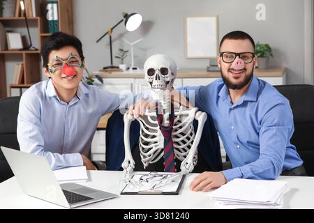 Collègues masculins avec déguisement drôle et squelette humain à table dans le bureau Banque D'Images
