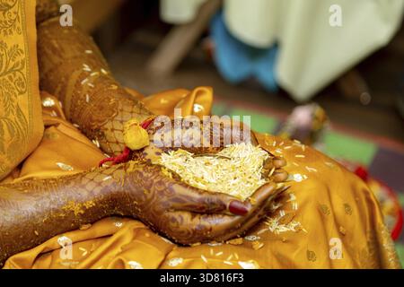 Les mains de la mariée sont ornées de henné et tiennent du riz pendant un rituel, symbolisant la prospérité et les bénédictions Banque D'Images