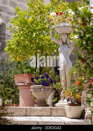 Gros plan d'une statue décorative en pierre blanche représentant une femme (peut-être une caryatide ou une nymphe de jardin) portant un bol de fleurs sur sa tête. La statue Banque D'Images