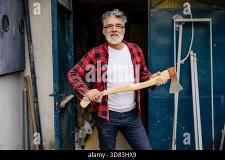 L'homme avec une hache se tient confiant devant un atelier Banque D'Images