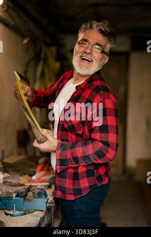 Homme souriant travaillant en atelier avec des outils et des matériaux en bois Banque D'Images