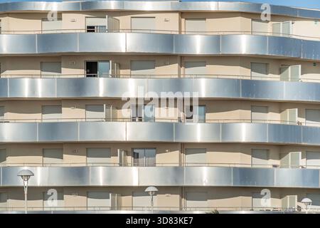 Gros plan de la façade d'un immeuble moderne incurvé avec fenêtres répétitives, murs beiges et balcons argentés métalliques Banque D'Images