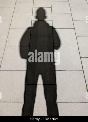 Silhouette longue d'ombre humaine sur trottoir pavé lumineux Cast by Low Sun créant un fond minimal de gens urbains Banque D'Images