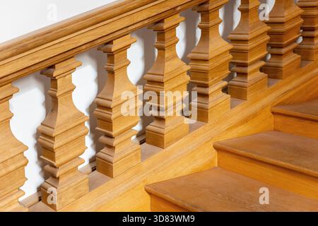 Les balustres en bois chauds forment un élégant motif répétitif le long de l'escalier dans la lumière du jour douce. Les surfaces lisses et les détails travaillés créent une atmosphère raffinée Banque D'Images
