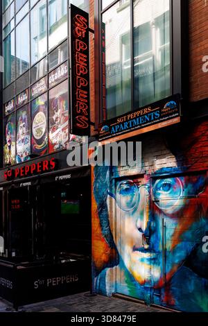 Liverpool, Angleterre - 10.08 2025 : vue sur la rue du lieu du Sgt Peppers avec une fresque murale de John Lennon et des affiches de fenêtre colorées. Scène urbaine du foie Banque D'Images
