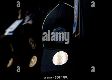 Manchester, Angleterre - 17.08.2025 : Casquette Manchester City sombre avec écusson brodé du club accroché dans un magasin. L'accessoire sportswear est allumé aga Banque D'Images