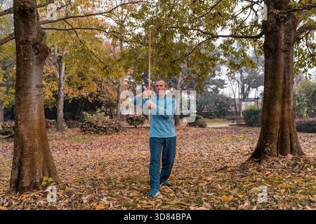 Homme faisant des exercices d'arts martiaux avec un bâton en bois parmi les feuilles tombées dans un parc Banque D'Images