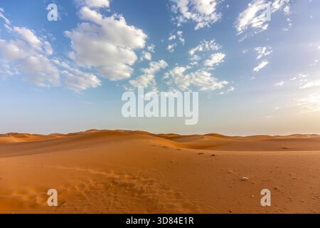 Lumière chaude du soir au-dessus des dunes de sable du désert de l'Erg Chebbi, Maroc, sous un ciel partiellement nuageux Banque D'Images