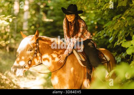 Rider souriant sur une jument Haflinger lors d'une promenade en sentier en forêt, lumière douce du soleil et atmosphère occidentale détendue || modèle libéré Banque D'Images