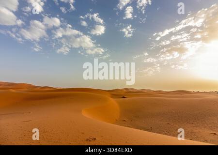 Lumière chaude du soir au-dessus des dunes de sable du désert de l'Erg Chebbi, Maroc, sous un ciel partiellement nuageux Banque D'Images
