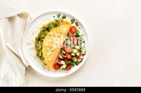 Omelette au brocoli rôti et fromage servi avec une salade de légumes frais sur assiette blanche sur fond clair avec espace copie. Alimentation saine Banque D'Images