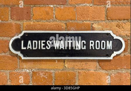 Panneau en métal coulé vintage lisant « Ladies Waiting Room » monté sur un mur rustique de briques rouges Banque D'Images