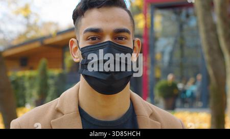 Gros plan homme hispanique dans le masque médical facial regardant le portrait de la caméra homme arabe dans le parc d'automne de la ville homme indien posant la pandémie covid19 malade Banque D'Images
