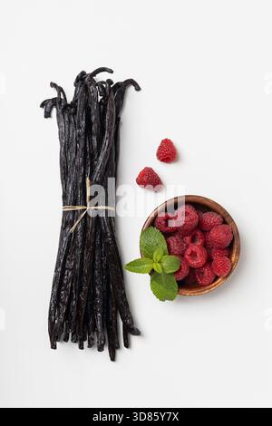 Haricots de vanille avec des framboises sur fond blanc. Bâtonnets de vanille secs. Banque D'Images
