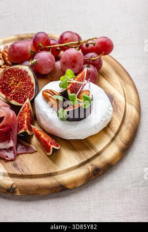 Camembert, fromage bree, noix, figues fraîches, raisins, prosciutto sur une assiette en bois. Assiette de charcuterie. Banque D'Images
