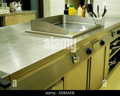 Comptoir de cuisine en acier inoxydable à l'intérieur du restaurant professionnel avec équipement de cuisine, bouteilles et ustensiles disposés pour la préparation des aliments en clea Banque D'Images
