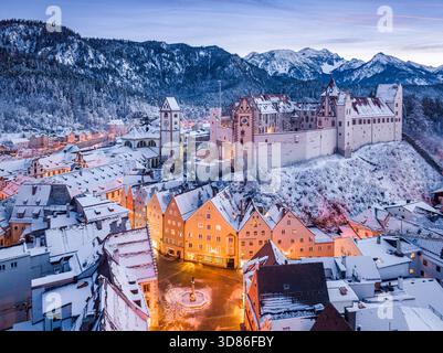 Vue aérienne de Hohes Schloss Füssen au sommet d'une colline poussiéreuse de neige, des lumières brillantes sur le ciel crépusculaire, entouré par la ville pittoresque et enneigée bel Banque D'Images