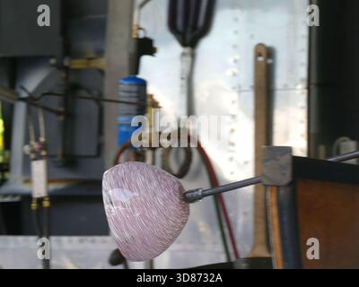 SEATTLE - APR 25, 2025 - souffleur de verre professionnel formant soigneusement des œuvres d'art en verre rose vif en utilisant une tige en métal et des techniques d'artisanat spécialisées dans Banque D'Images