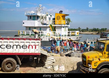 Scène portuaire fluviale animée avec des ouvriers chargeant la cargaison sur le bateau et les camions Banque D'Images