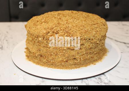 Un gâteau superposé magnifiquement conçu se trouve sur une planche à gâteau blanche. Le gâteau présente une garniture friable et une texture lisse, ce qui en fait un dessert invitant f Banque D'Images
